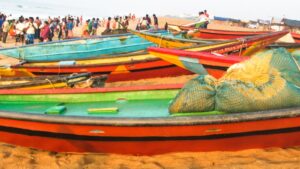 Brightly painted fishing boats pulled up on the beach at Puri in Odisha, with a crowd of fishers and villagers near the surf