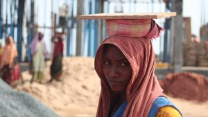 A woman construction worker carrying a wooden board on her head at a building site in Bhubaneswar, Odisha, the kind of daily-wage work covered by minimum wage rules