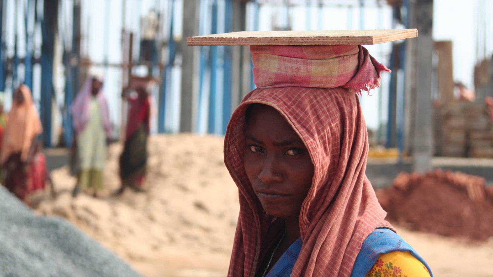 A woman construction worker carrying a wooden board on her head at a building site in Bhubaneswar, Odisha, the kind of daily-wage work covered by minimum wage rules