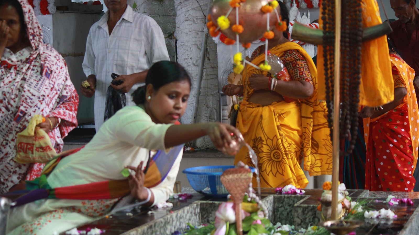 A young woman pours water as an offering during an early morning Mahalaya ritual at a Kolkata temple, with other devotees gathered around a decorated shrine
