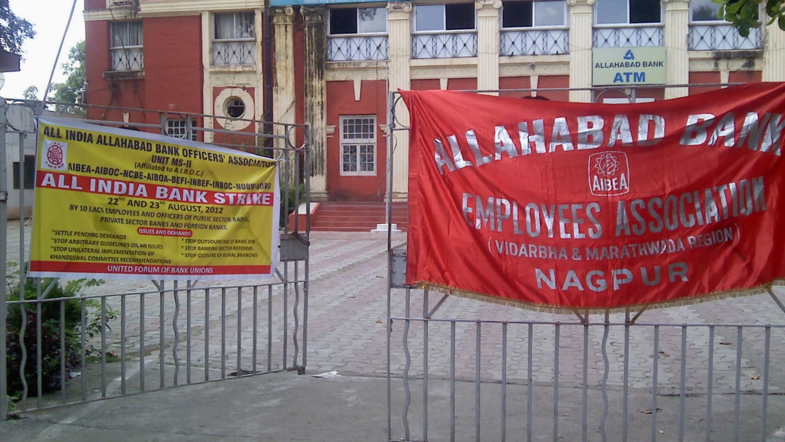 A red banner reading Allahabad Bank Employees Association AIBEA and a yellow All India Bank Strike notice from the United Forum of Bank Unions, tied to the gate outside a shuttered Allahabad Bank branch in Nagpur