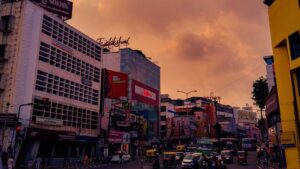 A busy evening street junction in Thiruvananthapuram, Kerala, under a dramatic orange sky, the city where the Onam Bumper lottery draw is held every year at Gorky Bhavan