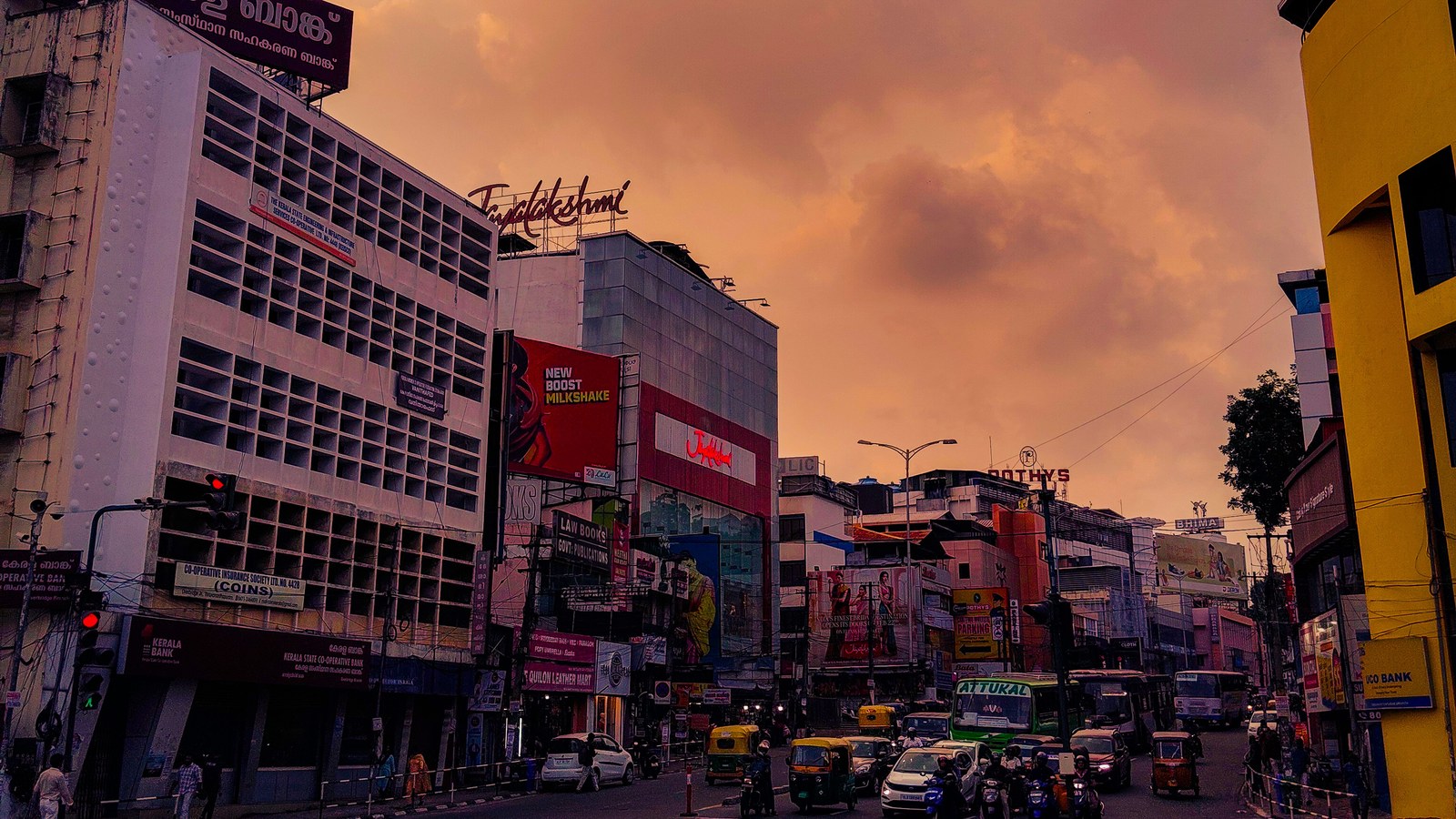 A busy evening street junction in Thiruvananthapuram, Kerala, under a dramatic orange sky, the city where the Onam Bumper lottery draw is held every year at Gorky Bhavan