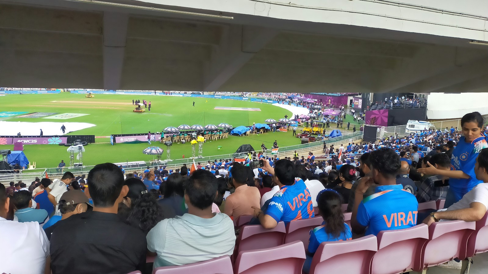 India cricket fans in blue team jerseys watching a match from the stands of an Indian cricket stadium