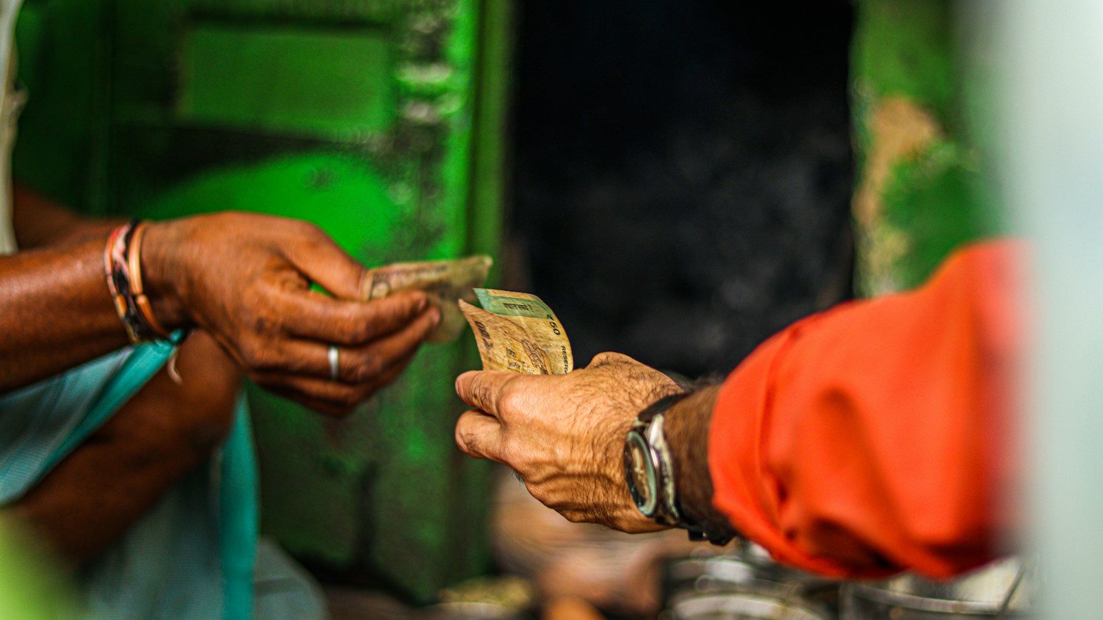 Two hands exchanging Indian rupee banknotes across a market stall counter